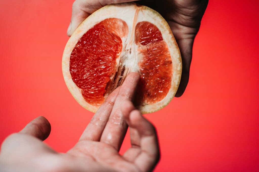 Erotische Kunstfotografie – Eine Hand berührt eine Grapefruit auf eine sinnliche Weise, symbolisiert weibliche Ejakulation.